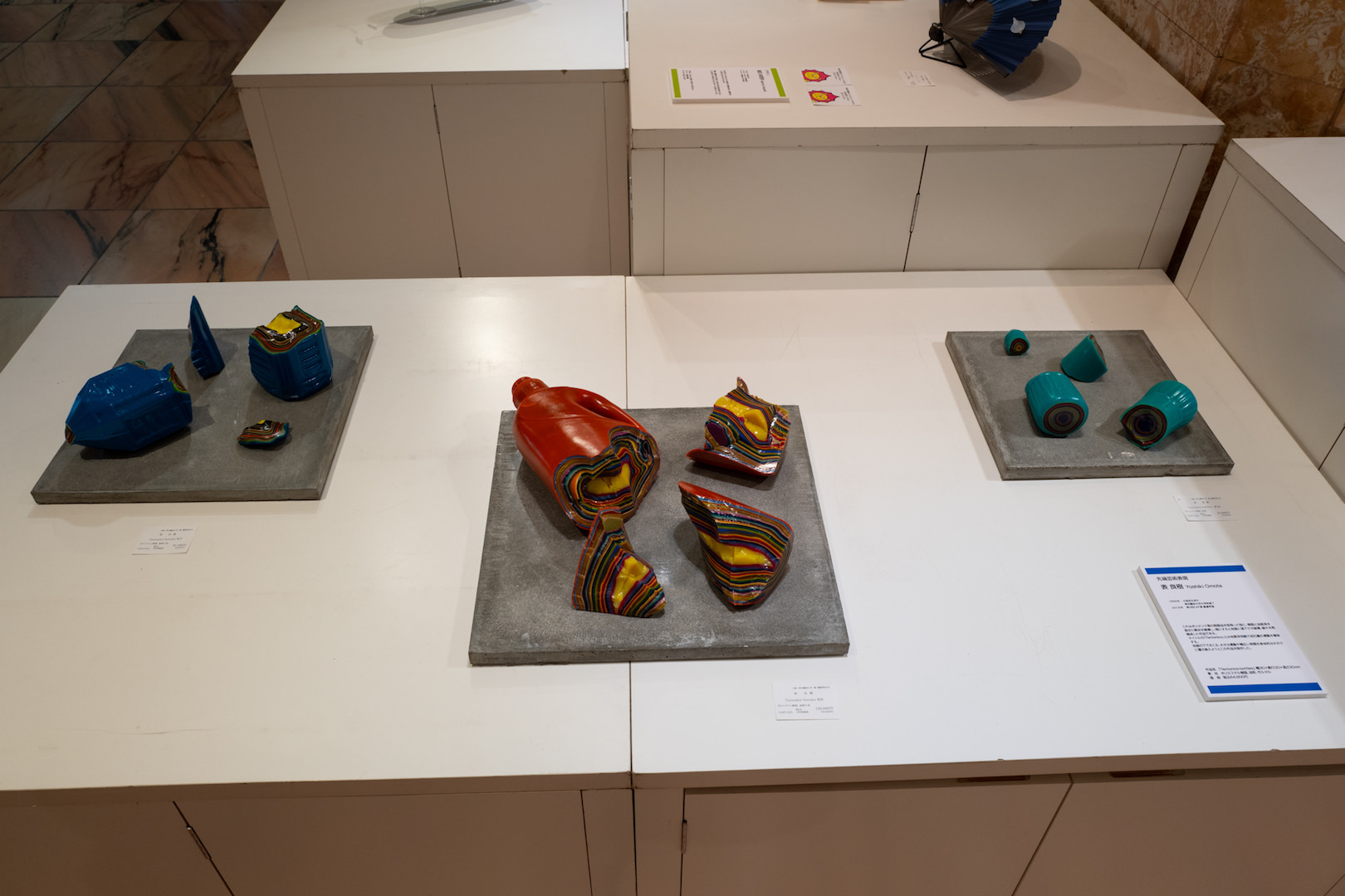 表良樹〜これはポリタンク等の既製品を型取った型に、樹脂と油絵具を混ぜた素材を積層し、塊にすると地面に落下させ破壊、破片を再構成した作品である。 タイトルの「Tectonics」とは地質学用語で岩石圏の運動を意味する。 地面の下でおこる、大きな運動や…