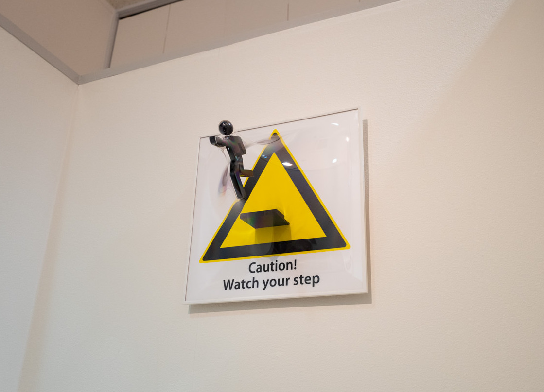中地下から地下へと階段を降りる際《Watch your step》という注意喚起のサイン。作品に気をとられると危険です。