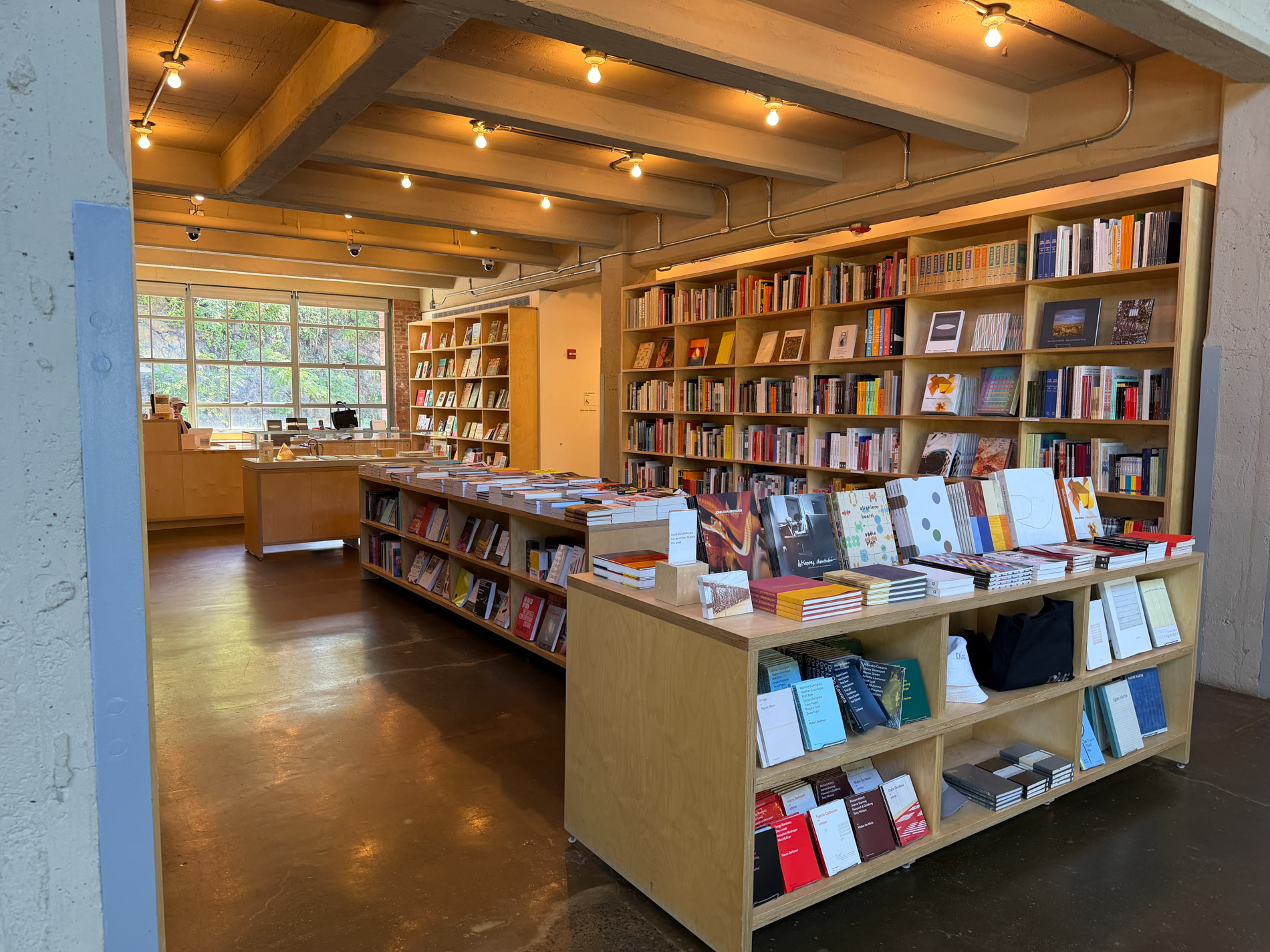 木の本棚と平台に美術書がぎっしり並ぶ書店。奥に窓がある
