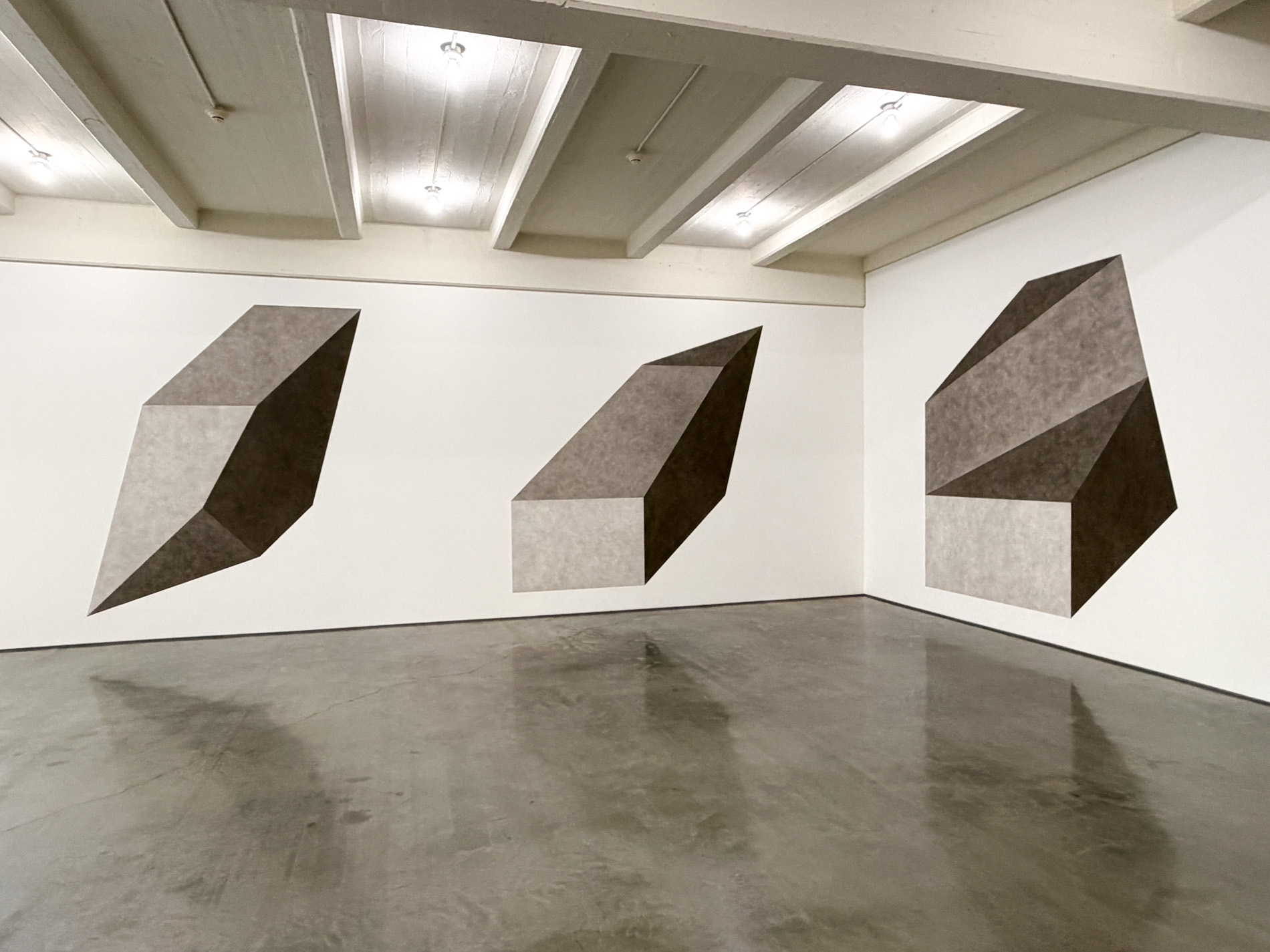 白い壁3面に、灰色の濃淡で塗り分けた大きな多面体が一つずつ描かれている。床は灰色のコンクリート