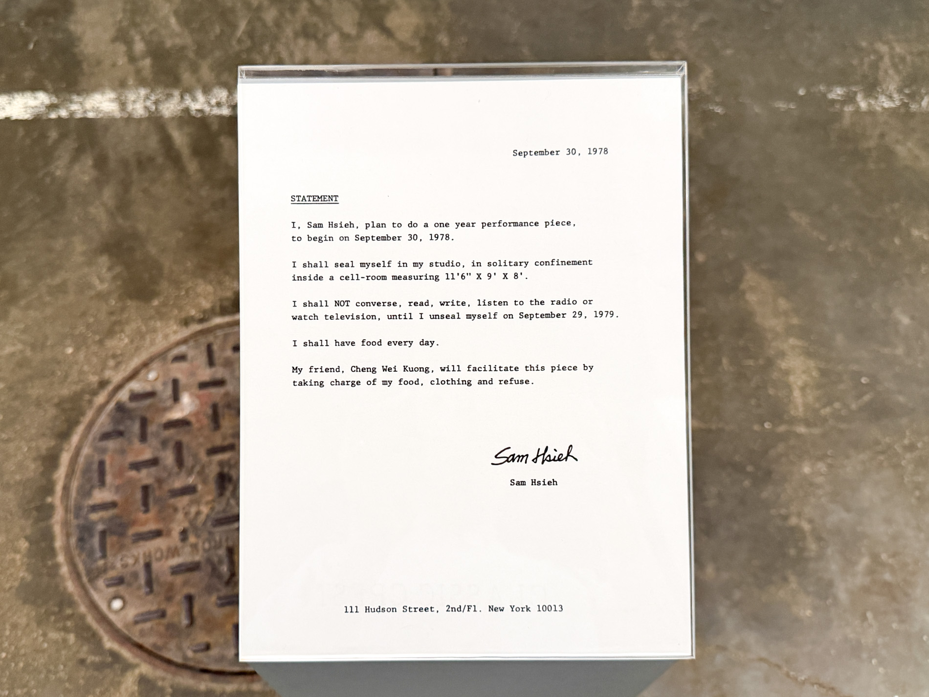 コンクリートの床に置かれた台の上の、タイプライターで打たれた英文の書類。末尾に Sam Hsieh の署名がある