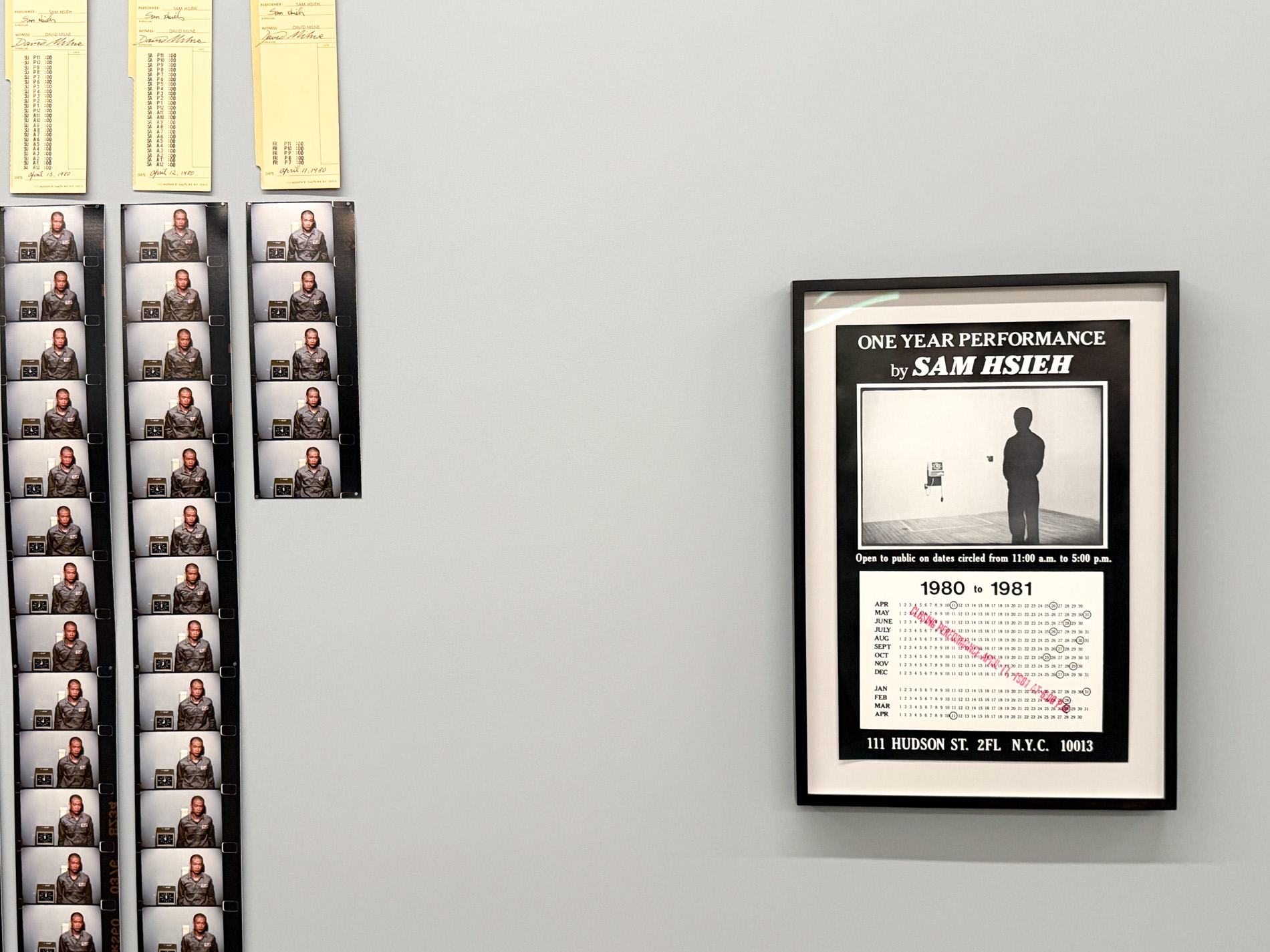 壁の左に黄色いタイムカード3枚と、その下に縦に続くフィルムのコマ。右に「ONE YEAR PERFORMANCE by SAM HSIEH」と書かれた額装のポスター