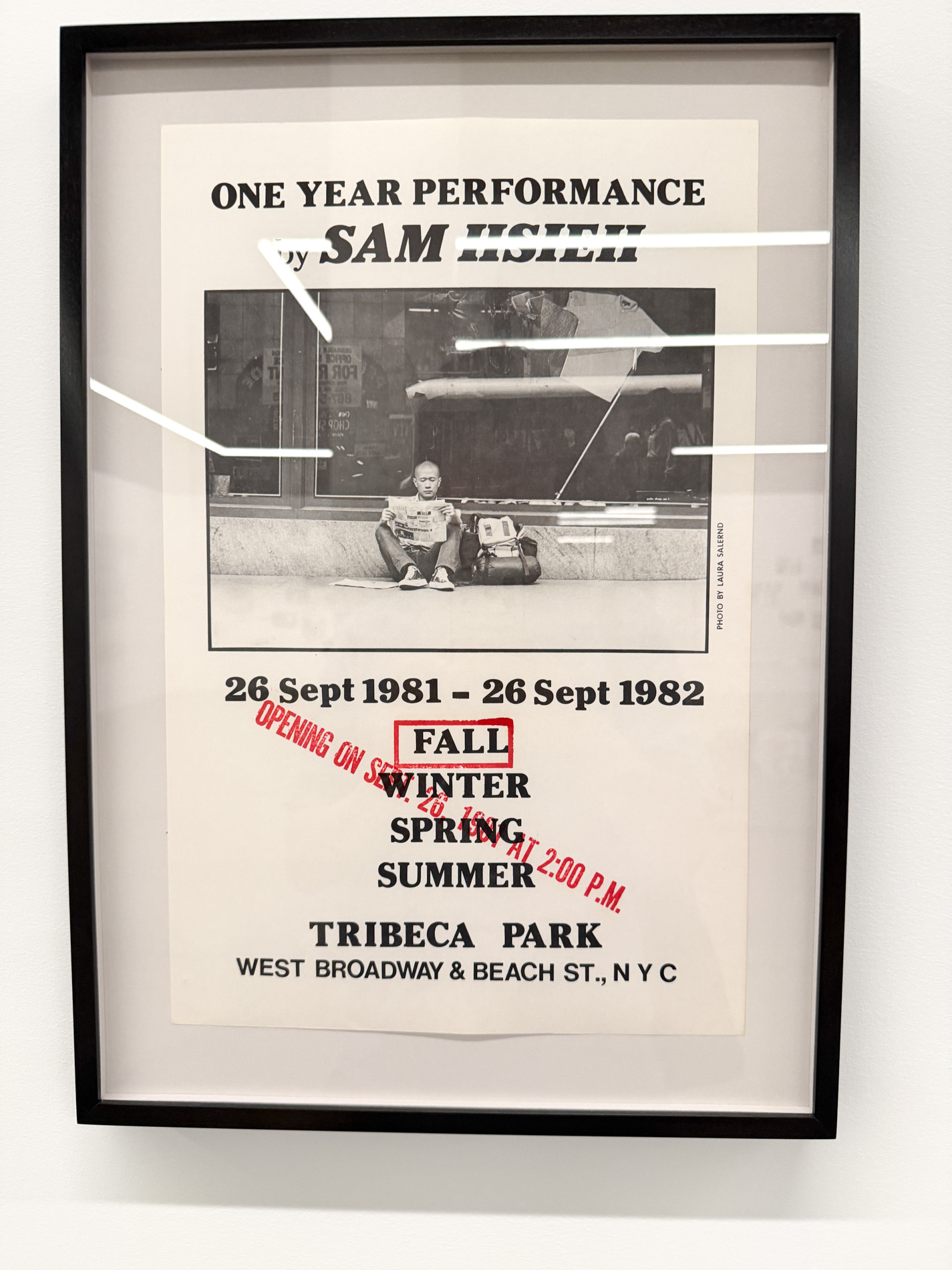 額装のポスター。上に「ONE YEAR PERFORMANCE by SAM HSIEH」、中央に歩道に座る男性の白黒写真、下に「26 Sept 1981 – 26 Sept 1982」「TRIBECA PARK」の文字