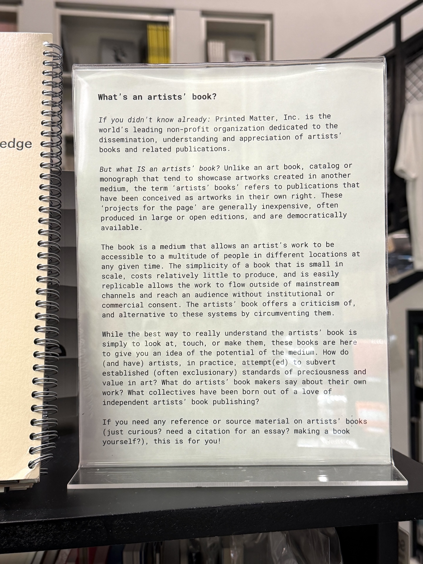 透明なアクリルのスタンドに入った英文の説明書き。見出しは「What's an artists' book?」