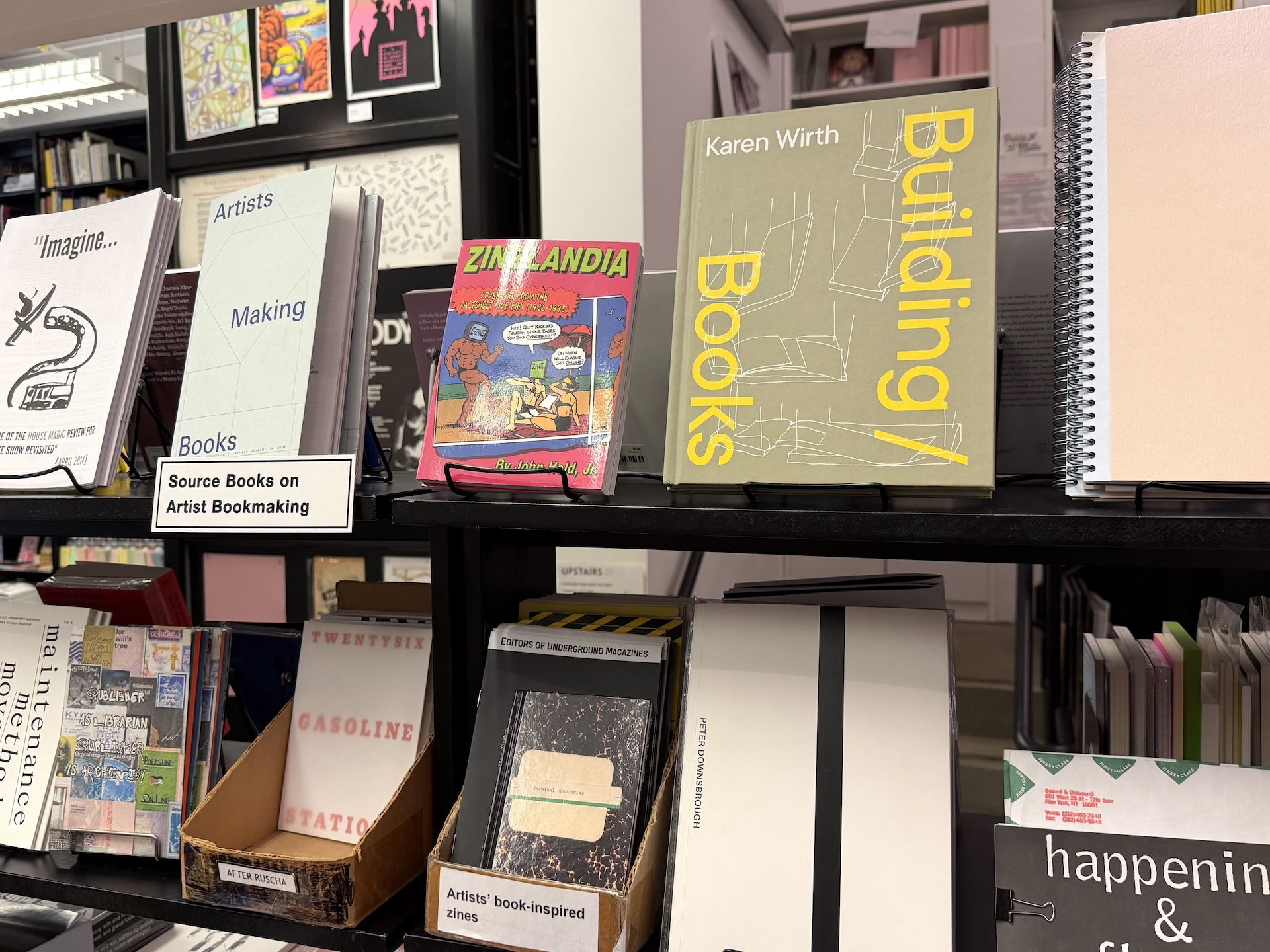 棚の下段に「After Ruscha」と書かれた段ボールの箱があり、『Twentysix Gasoline Stations』の表紙が見える。上段には本づくりに関する本が並ぶ
