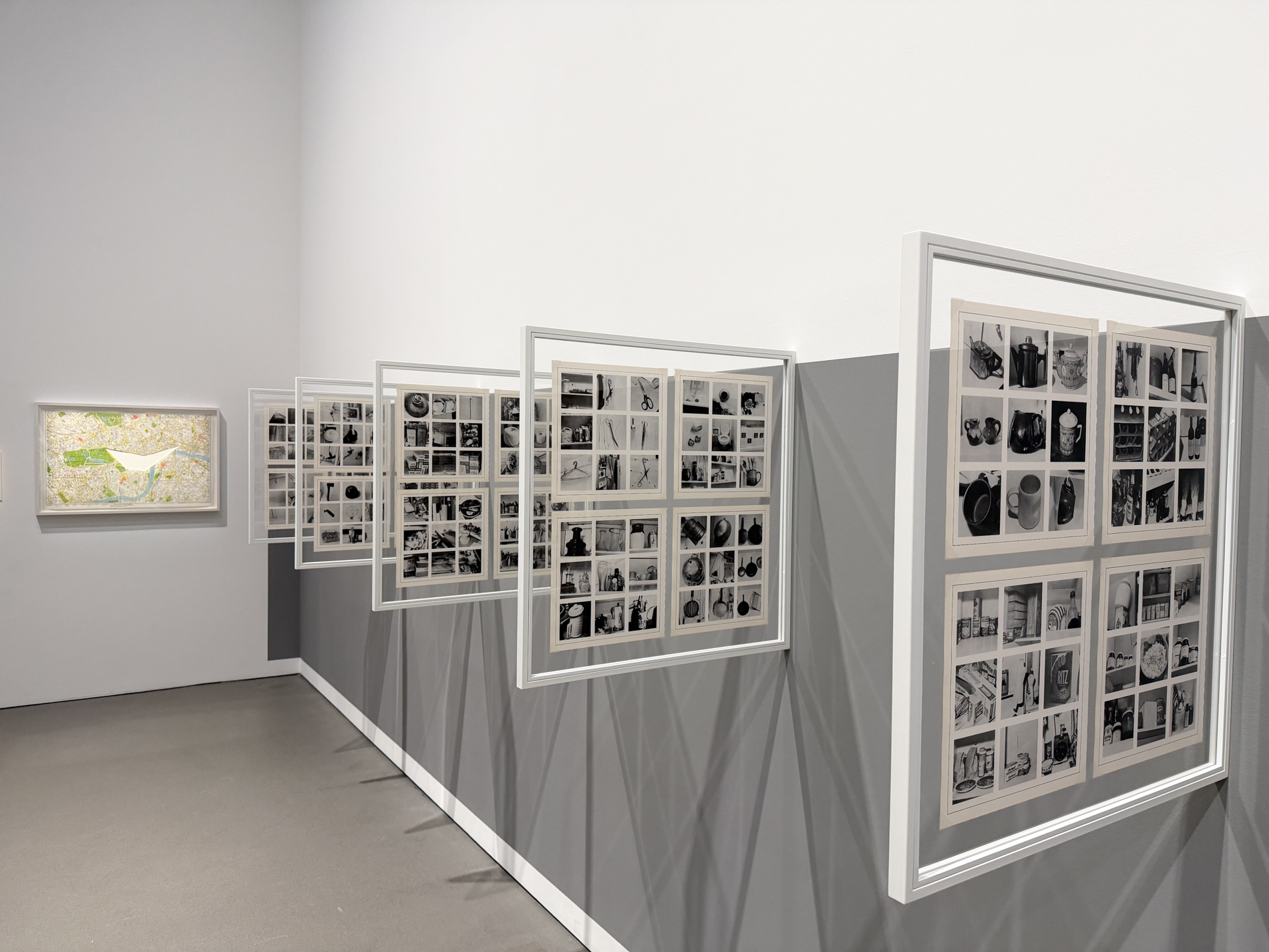 展示室の壁に、地図を用いた作品と、白黒写真をグリッド状に並べた額装作品が斜めに連なって掛かる