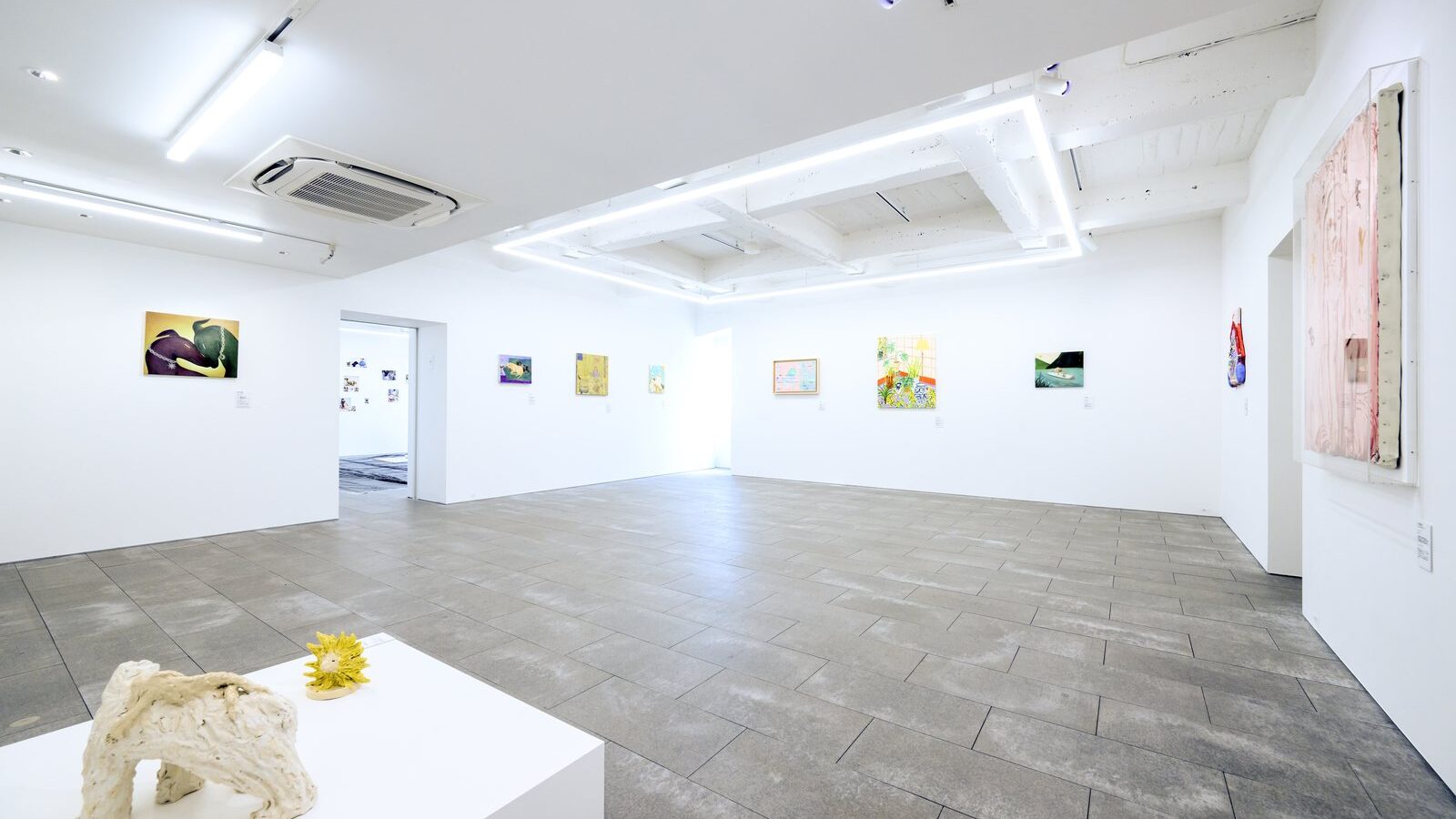 白い展示室の全景。手前の白い台に陶の犬の立体、奥の壁に作家たちの新作が並ぶ