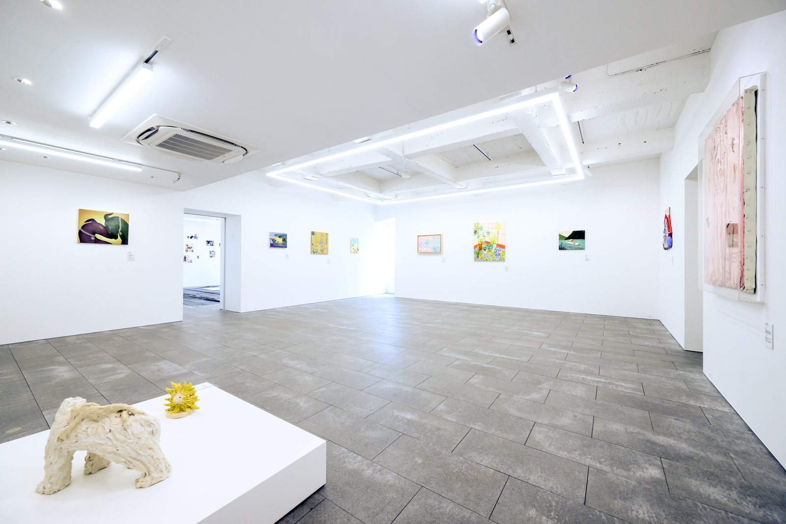 白い展示室の全景。手前の白い台に陶の犬の立体、奥の壁に作家たちの新作が並ぶ