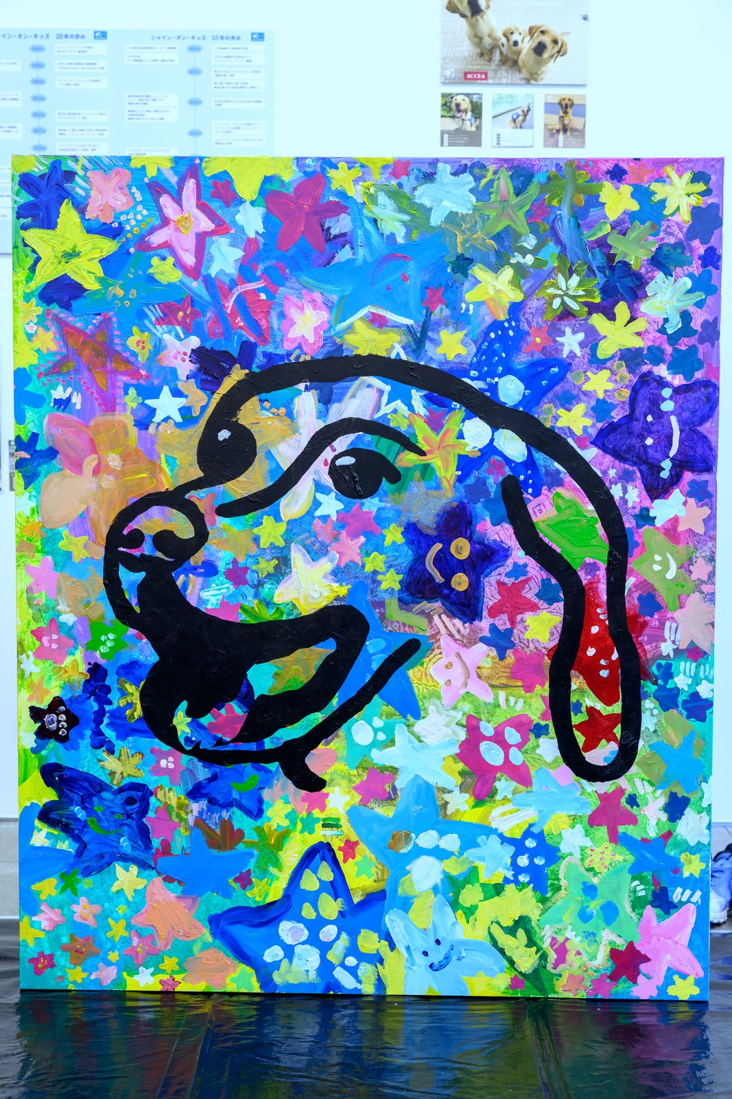 星と花で埋め尽くされた画面に、黒い太い線で犬が1頭描かれた100×120cmの共同制作作品
